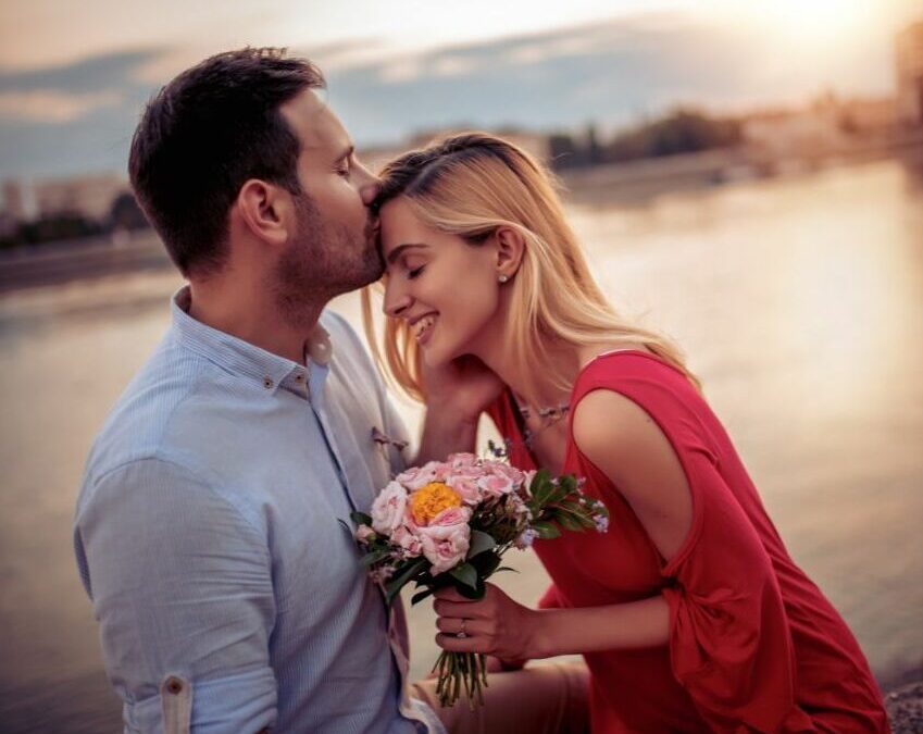 Mann küsst Frau auf Stirn und sie hält Blumen von ihm in der Hand, so entfacht man Liebe neu